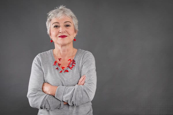 Selbstbewusste ältere Frau mit verschränkten Armen vor grauem Hintergrund